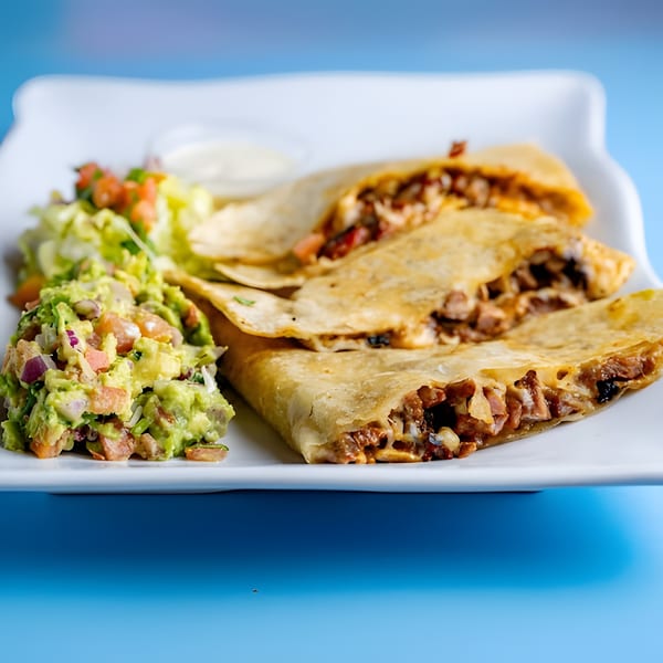 Three Baja California Tacos quesadillas with guacamole, salsa, and sour cream on a white plate.