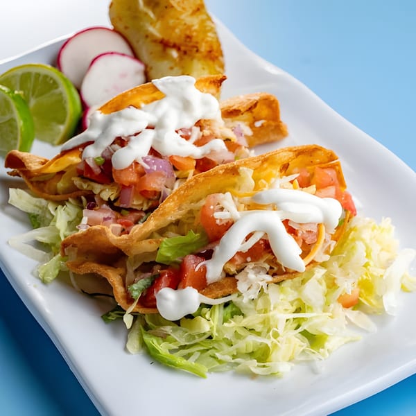Two crispy Baja California Tacos with lettuce, tomato, cheese, and sour cream, served with lime and radishes.