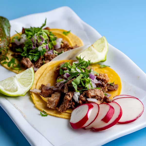 Two Baja California Tacos with meat, cilantro, and onions, served with lime and radish slices.