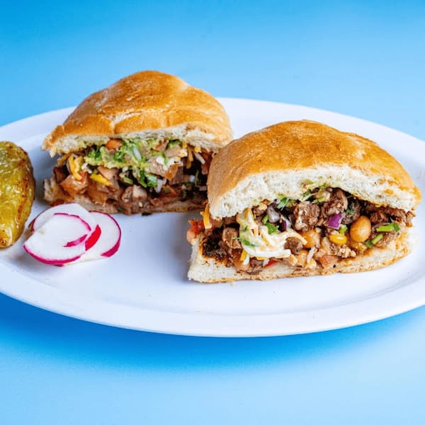 Two Baja California Tacos tortas, filled with meat and vegetables, served with radishes and a pepper.