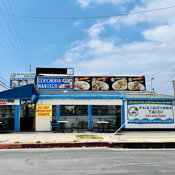 Exterior of Baja California Tacos, a blue and white building with outdoor seating and menu signs.