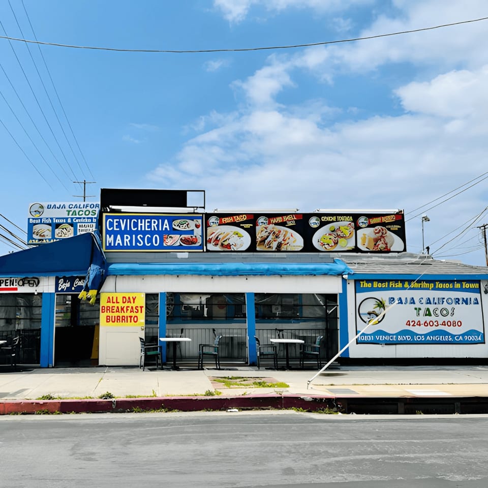 Exterior of Baja California Tacos, a blue and white building with outdoor seating and menu signs.