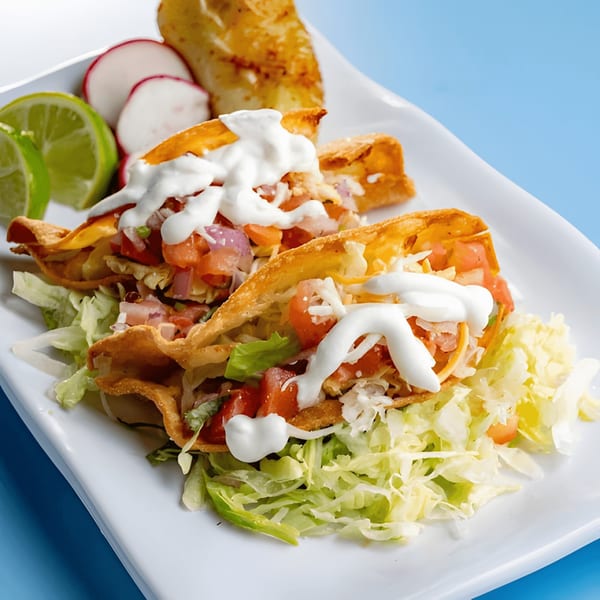 Two crispy Baja California Tacos with shredded lettuce, diced tomatoes, and sour cream, served with lime and radishes.