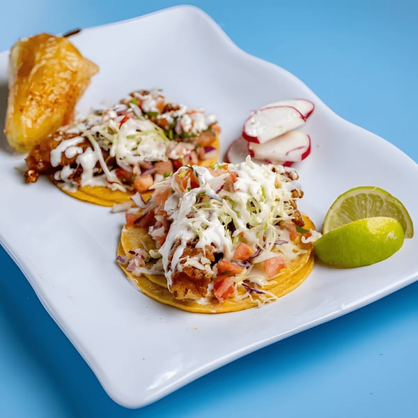 Two Baja California fish tacos with cabbage, pico de gallo, and crema, served with lime and radishes.