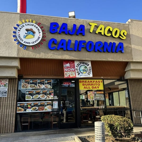 The exterior of Baja California Tacos, featuring a blue and yellow sign and menu displays.